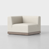 A modern, cream-colored corner armchair with a minimalist design and a wooden base, placed on a smooth, light gray floor against a plain white background.
