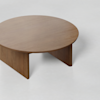 A round wooden coffee table with a smooth surface and three thick, flat legs, placed on a light-colored floor.