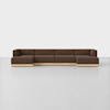 A modern, modular brown sectional sofa with wooden bases sits on a plain white floor against a white background. The sofa has clean lines and seats five or more people.