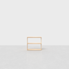 A small, light wood, two-tiered open shelf sits alone on a smooth, light gray floor with a plain white background.