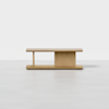 A minimalist wooden coffee table with clean lines, a flat rectangular top, an offset supporting panel, and an open shelf underneath, set against a plain white background.