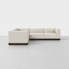 A modern L-shaped sectional sofa with cream-colored upholstery and a dark wooden base, placed in a minimalistic, empty room with a light gray floor and white walls.