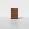 A modern, minimalist five-drawer wooden dresser stands alone on a light grey floor against a plain white background.