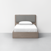 A simple bed with a light wood frame, gray padded headboard, white bedding, and a single white pillow, placed against a plain white wall in a minimalist room.