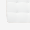 A close-up of the corner of a white, quilted mattress with stitched tufting and a fabric edge against a plain background.