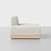 Side view of a modern, minimalist cream-colored sofa with a low wooden base and a single backrest, placed on a light gray floor against a plain white background.