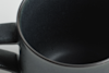 Close-up view of the inside of a dark, empty ceramic mug, with the handle partially visible on the left side against a light background.