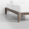 A close-up of a minimalist wooden bed frame with a light brown finish, supporting a mattress and white bedding in a modern, clean room with a gray floor and white wall.