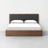 A modern wooden bed frame with a dark gray upholstered headboard, neatly made with white bed linens and two pillows, set against a plain white wall and gray floor.