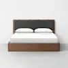 A modern wooden bed frame with a dark gray upholstered headboard, neatly made with white bed linens and two pillows, set against a plain white wall and gray floor.