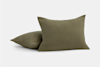 Two olive green, textured throw pillows with a subtle checkered pattern are placed on a plain light gray background. One pillow is upright while the other lies flat behind it.