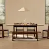 Minimalist dining room with a long wooden table, four wooden chairs, a wooden bench, beige curtains, and a large abstract painting with black shapes on the wall behind the table.
