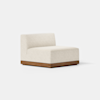 A modern, armless lounge chair with cream-colored upholstery and a low wooden base is placed on a smooth light gray floor against a plain white background.