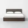 A modern bed with a dark brown wooden frame, a gray upholstered headboard, and white bedding with two pillows, set against a plain white wall and gray floor.