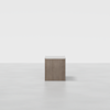 A single, square wooden pedestal stands centered on a smooth, light gray surface with a plain white background.