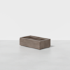A rectangular, wooden drawer box with smooth, flat surfaces sits on a light gray floor against a plain white background.