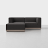 A modern, dark gray sectional sofa with clean lines, low backrests, and wooden base, positioned in a minimal, light-colored room with a plain background.
