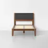A modern wooden bed frame with a tall, upholstered dark gray fabric headboard and wooden slats, set against a plain white wall and light gray floor.