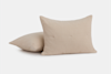Two beige rectangular pillows with a textured, quilted fabric rest on a white surface; one pillow is upright while the other lies flat in the background.