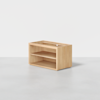 A small, rectangular wooden shelf unit with two open shelves, placed on a light gray floor against a plain white background.