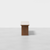 A minimalist wooden table with a light-colored rectangular top and a solid central base, set against a plain white background.