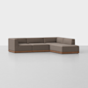 A modern, L-shaped sectional sofa with brown upholstery and a wooden base, placed on a light gray floor against a plain white background.
