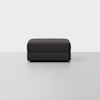 A square, dark gray upholstered ottoman sits on a light, seamless floor against a plain white background.