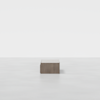 A minimalist, rectangular wooden coffee table sits alone in a bright, empty space with a white background and floor.