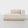 A modern, minimalist beige chaise lounge with a low wooden base and right-side armrest, set against a plain white background.