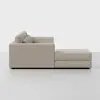 A side view of a modern, light beige sectional sofa with plush cushions and an attached chaise lounge, set against a plain white background.