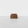 A small, square wooden storage box with open compartments sits on a light gray floor against a plain white background.