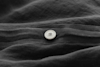 A close-up of a white button sewn onto black or dark gray fabric with visible stitching and soft folds in the material.