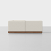A modern, minimalist sofa with light beige upholstery and a wooden base, viewed from the back against a plain, light gray background.