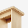 Close-up view of the corner of a light wood table with smooth, rounded edges and a soft, neutral-colored padding on top. The photo highlights the craftsmanship and finish of the furniture.