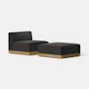 A modern, minimalist black upholstered chair with a low back and matching ottoman, both featuring light wood bases, set against a plain white background.