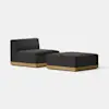 A modern, minimalist black upholstered chair with a low back and matching ottoman, both featuring light wood bases, set against a plain white background.