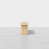 A minimalist wooden bench with a slot down the center, photographed from the end against a plain white background on a smooth, light gray floor.