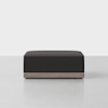 A modern, rectangular ottoman with a dark upholstered cushion and a light wooden base, set on a light, minimalist background.