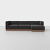 A modern dark gray sectional sofa with clean lines and a wooden base, placed in a minimal, white room with a light gray floor.
