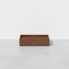 A plain, rectangular wooden box with an open top sits on a smooth, light gray surface against a white background.