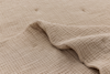 A close-up of a textured beige blanket or quilt with a raised, crinkled pattern and part of the edge lifted, showing its soft, fabric detail.