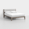 A modern bed with a light wood frame, angled legs, and a padded gray headboard. The bed is neatly made with white sheets, two pillows, and is set against a plain white wall and floor.