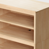 A close-up of a light wood bookshelf showing three shelves, with one shelf featuring a small circular hole at the back for cable management. The surface appears smooth and unpolished.