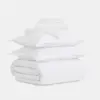 A neatly folded white bedding set, including a duvet, two pillows, and stacked sheets, arranged against a plain white background.