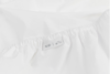 A close-up of a white fitted sheet showing an elastic edge and a fabric tag with simple black symbols, including a chain link and an arrow pointing upward.