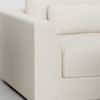 Close-up view of a modern beige upholstered armchair with textured fabric, showing the armrest, seat cushion, and part of the backrest on a light-colored floor.