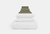 A neatly stacked bedding set on a white background, featuring folded green sheets and pillowcases on top of two white pillows and a rolled white comforter at the bottom.