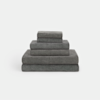 A neatly stacked set of dark gray towels in various sizes arranged from largest on the bottom to smallest on top, against a plain white background.
