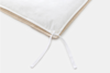Close-up of the corner of a white duvet with a visible fabric tie, lying on top of a beige blanket, against a light gray background.