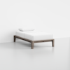 A minimalist single bed with a light wooden frame, white mattress, sheet, and pillow, placed in a bright, empty room with white walls and floor.